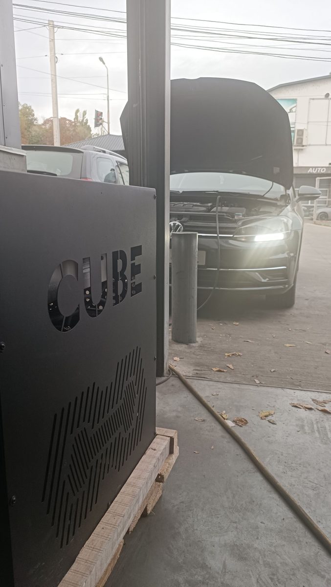 Аппарат CUBE во дворе, за ним машина с открытым капотом во время очистки